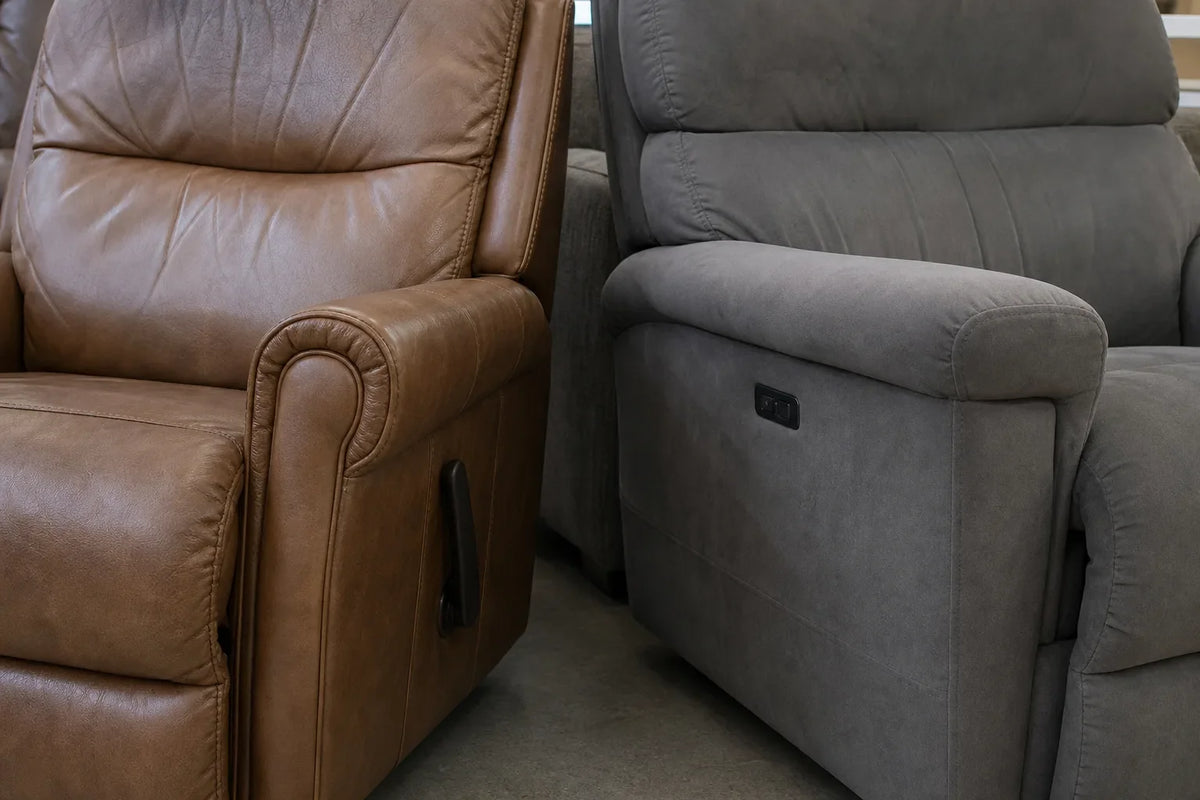 Close-up of a brown leather manual recliner with a side lever beside a grey fabric power recliner with control buttons