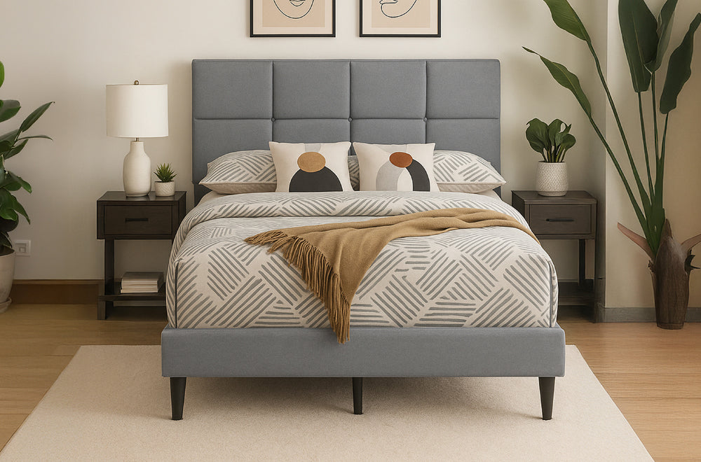 Gray upholstered bed with a panel-tufted headboard, low footboard, and dark tapered legs in a modern bedroom.