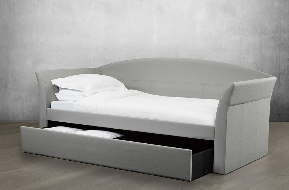 Grey upholstered Starboard Daybed with curved back and open storage drawer holding pillows