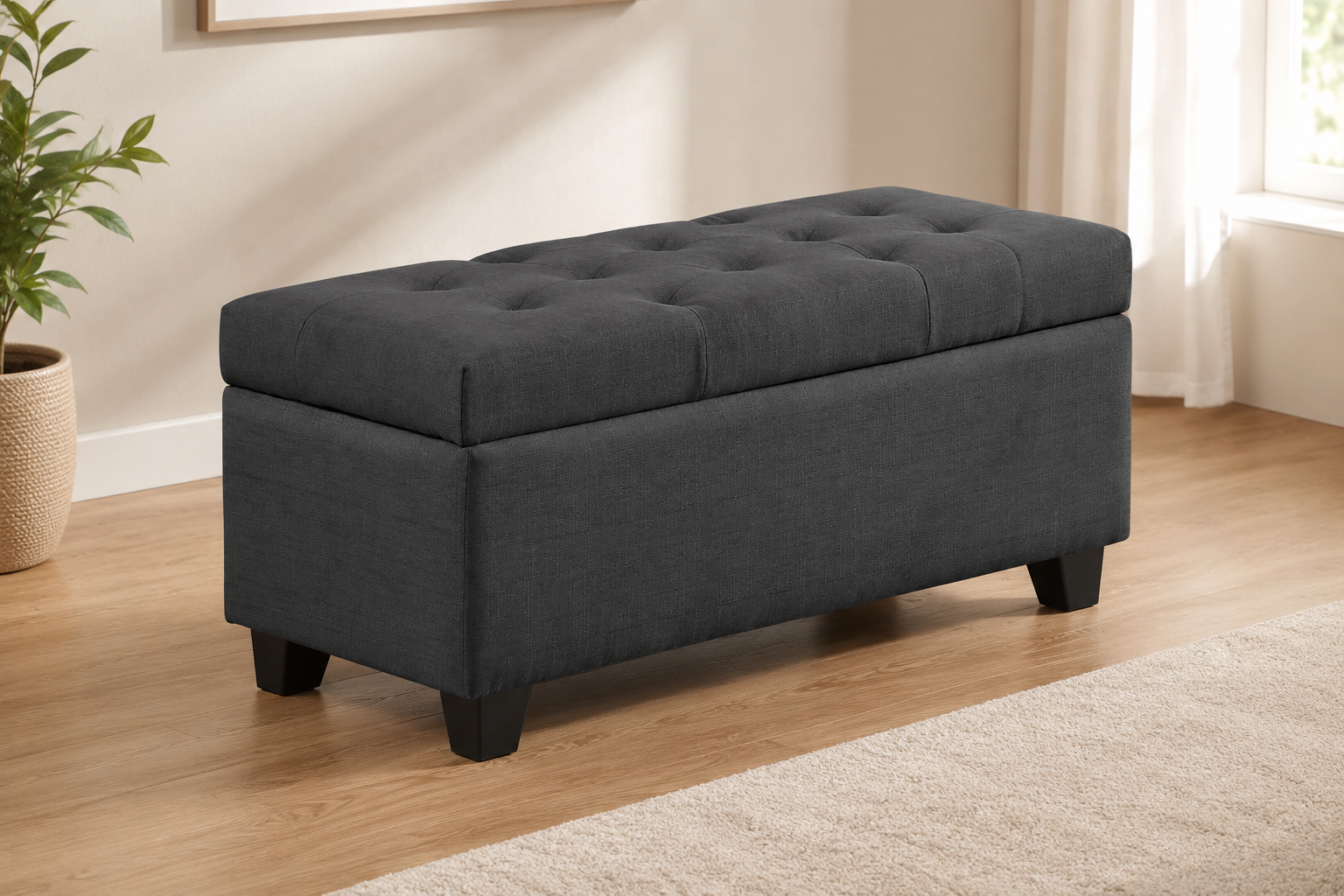 Charcoal gray fabric storage bench with a button-tufted cushioned lid and dark tapered legs in a modern neutral room.