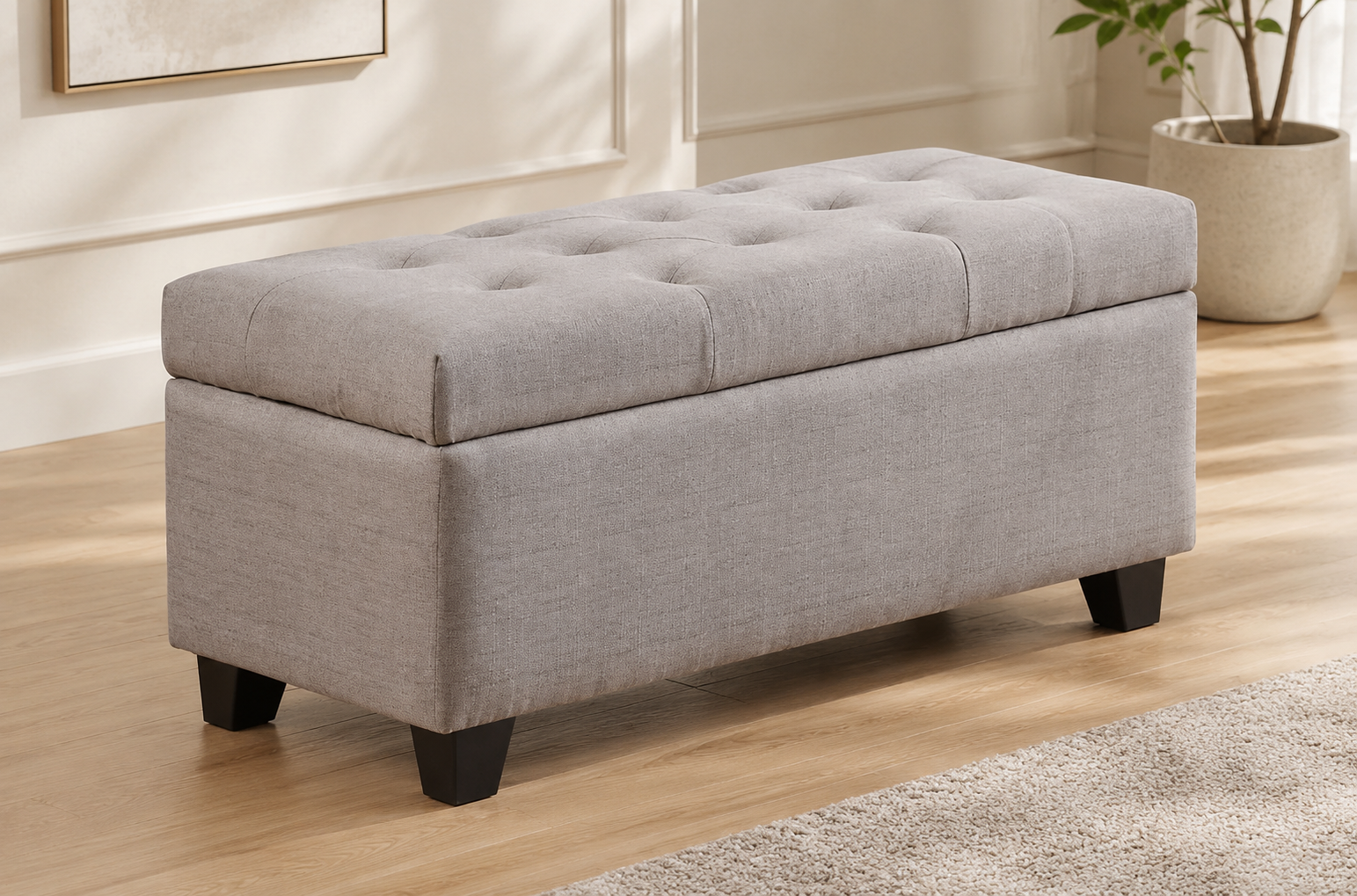Light taupe fabric storage bench with a button-tufted cushioned lid and dark tapered legs in a modern neutral room.