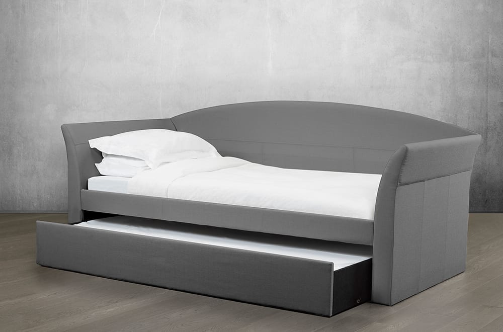 Starboard Daybed in muted grey fabric at an angle with trundle drawer partly pulled out against a textured grey wall