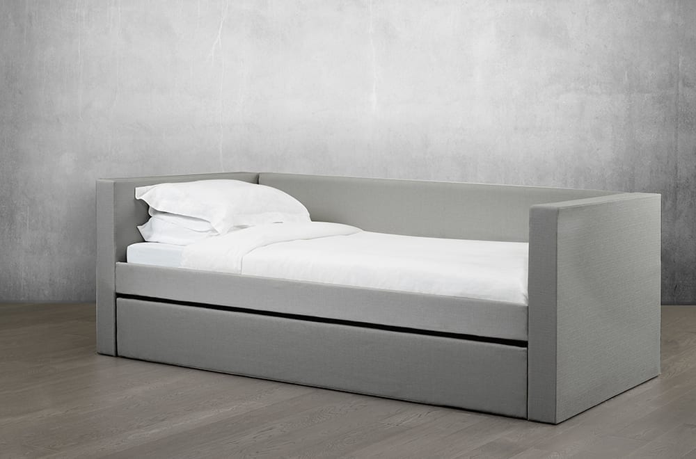 Bowsprit Daybed in soft light grey seen at an angle with bedding and trundle partially extended on a hardwood floor