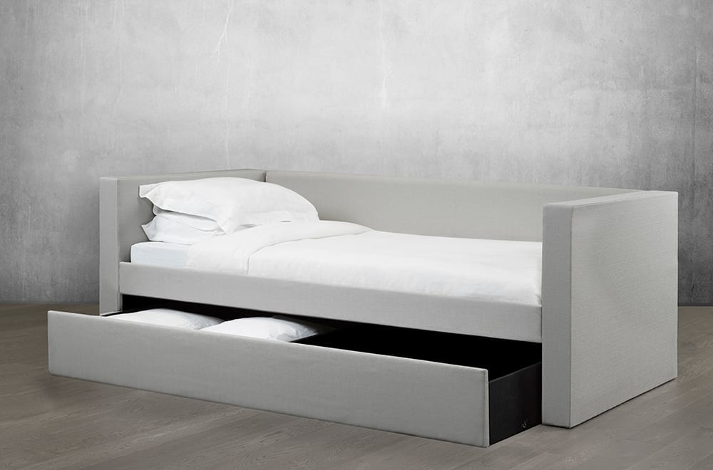 Bowsprit daybed in light fabric seen from the foot of the bed with storage drawer pulled out showing pillows inside