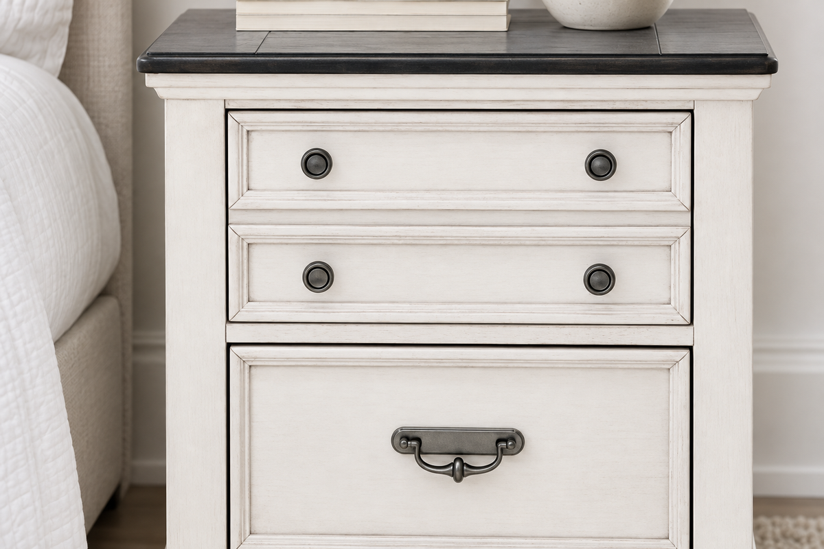 Close-up of the Natasha antique white nightstand showing drawer fronts, round knobs, a metal handle and the contrasting dark top.